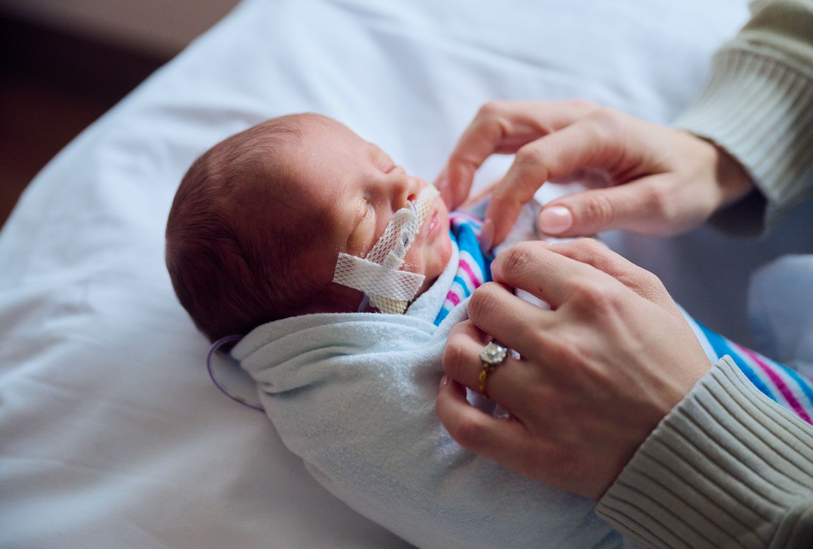 Hands tending to tightly wrapped newborn baby
