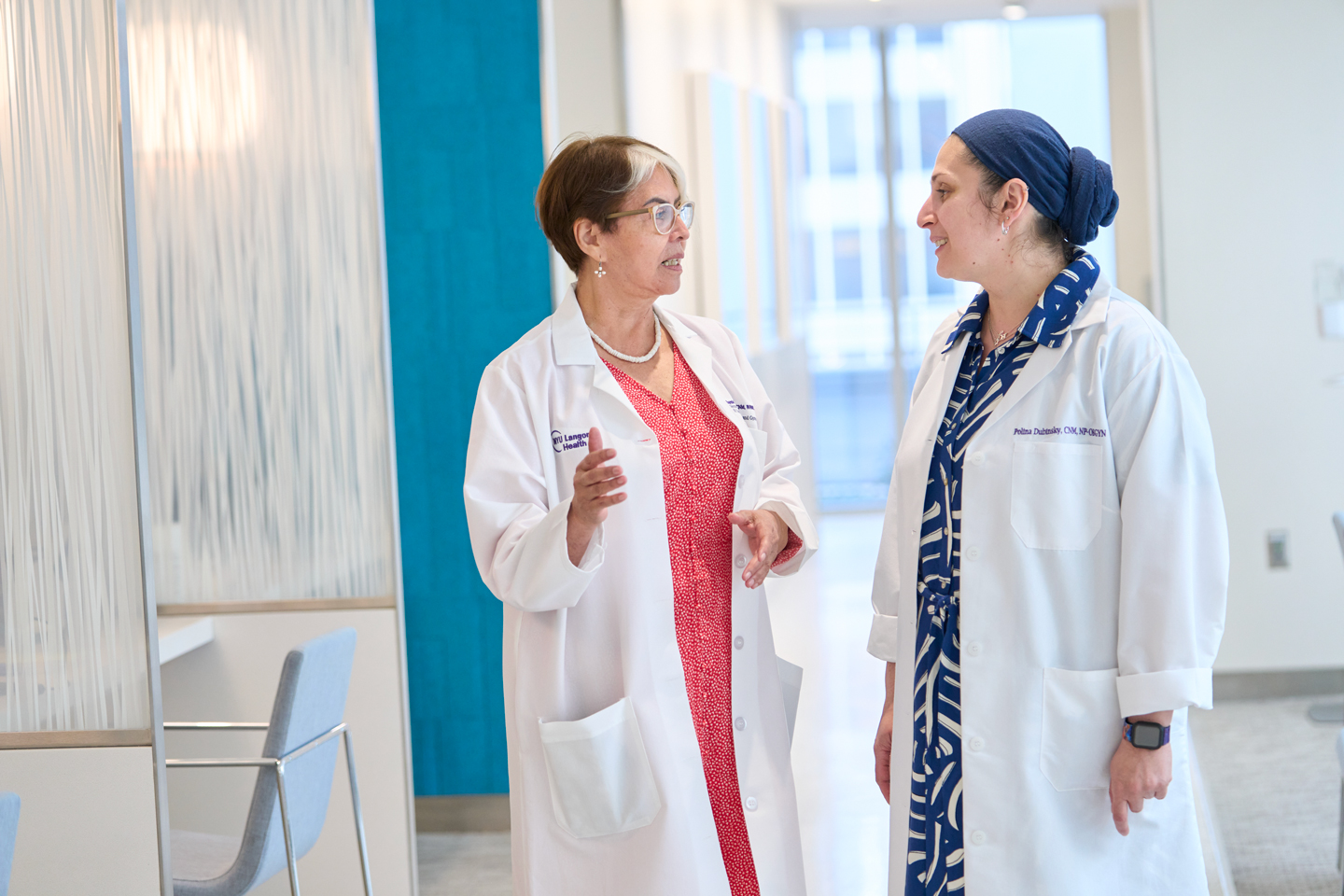 Midwives Eugenia Montesinos and Polina Dubinsky wearing white coats and talking together in clinical setting