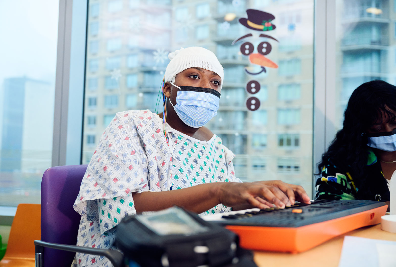 Patient wearing gown and face mask playing keyboard