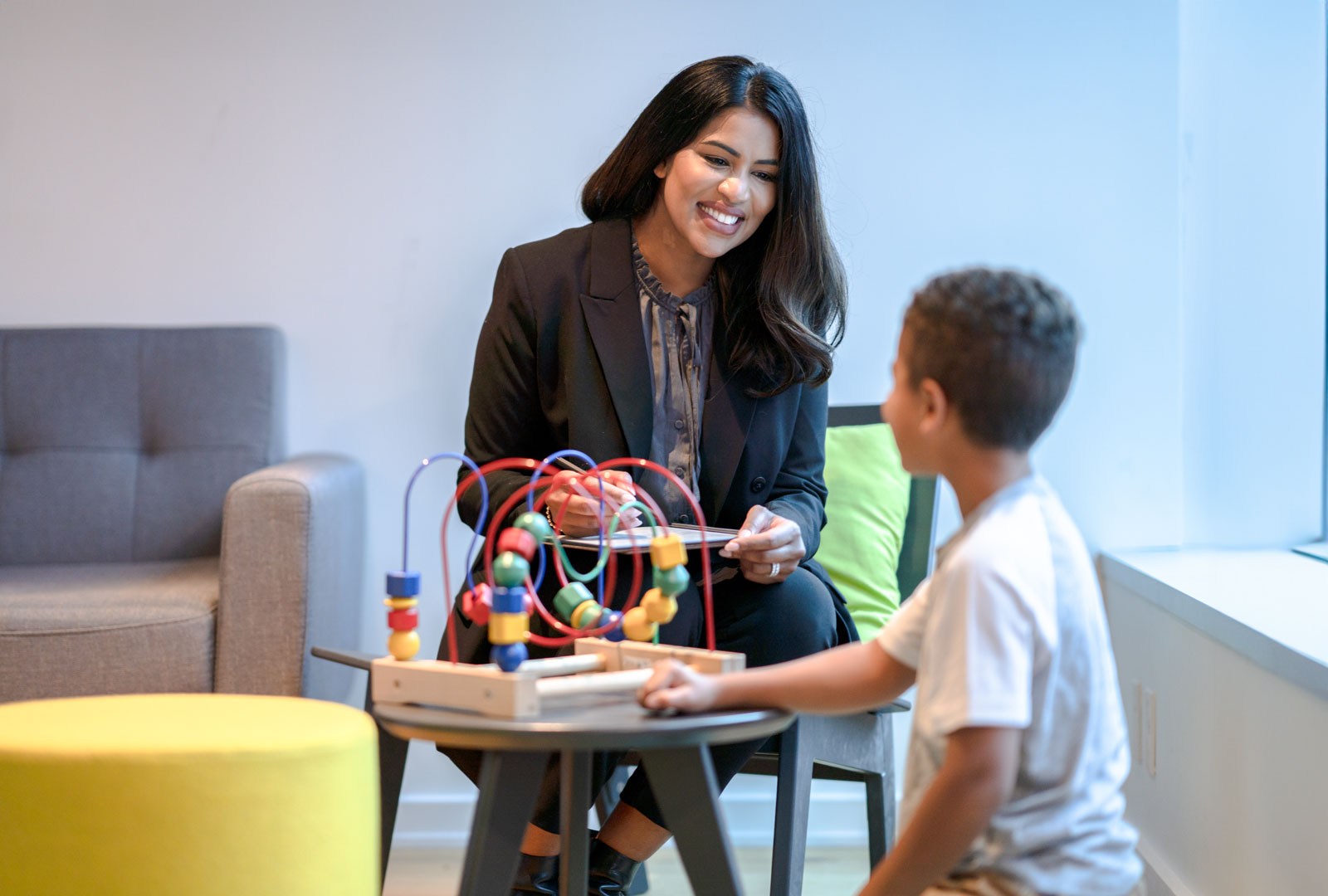 Smiling provider looking on at child seated on ground playing with toy